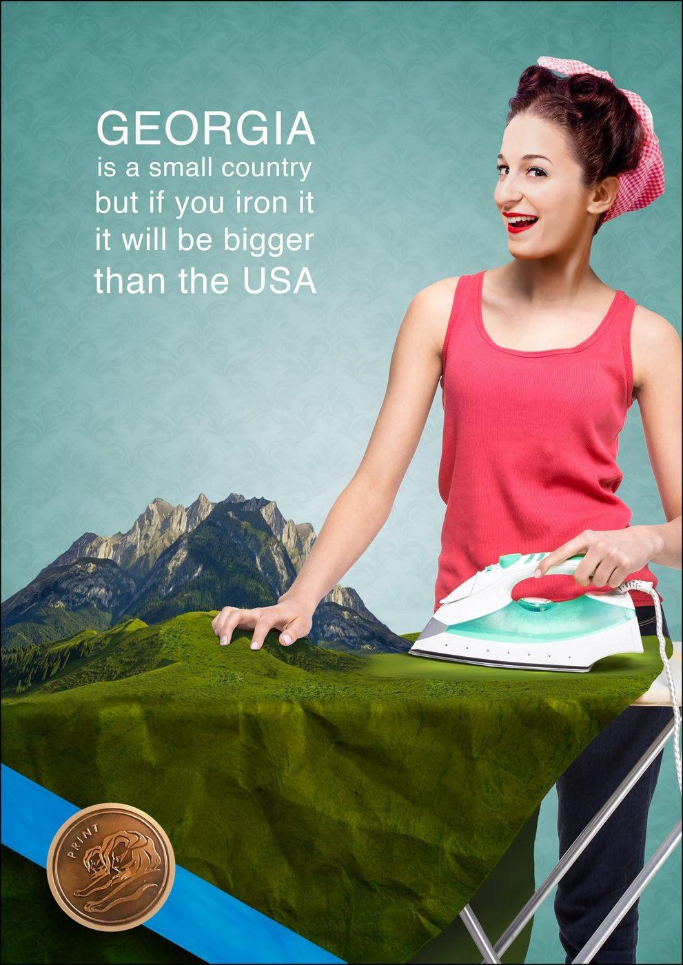 Print ad: a woman irons a mountain landscape on an ironing board; Georgia is a small country but if you iron it, it will be bigger than the USA